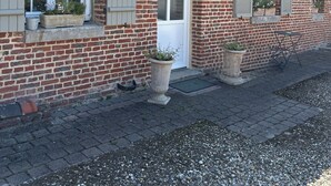 A brick building with a white door, windows with shutters, and potted plants on the windowsills.