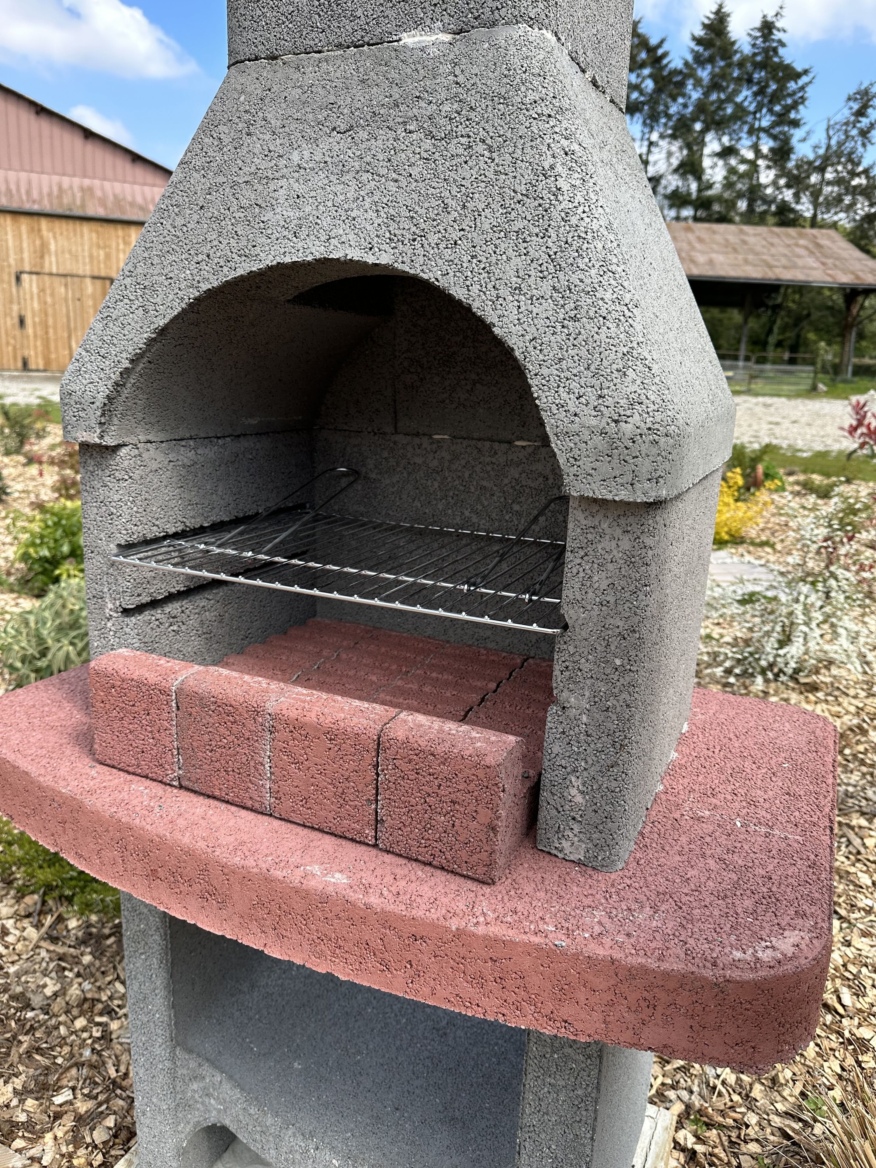 A stone-built outdoor oven with a metal rack inside, set on a brick base with a red top.