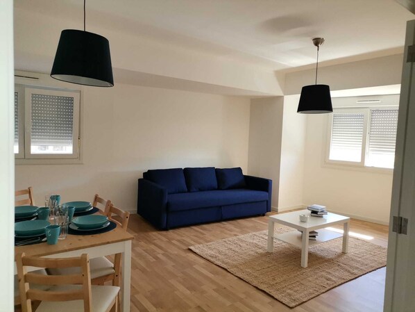 A living room with a blue sofa, a dining table with teal chairs, and a white coffee table. - APARTMENT 1 (Vila Nova de Gaia)