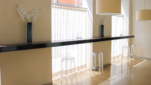 Un espace bar moderne avec un comptoir noir, des tabourets transparents et deux vases ornés de fleurs blanches.