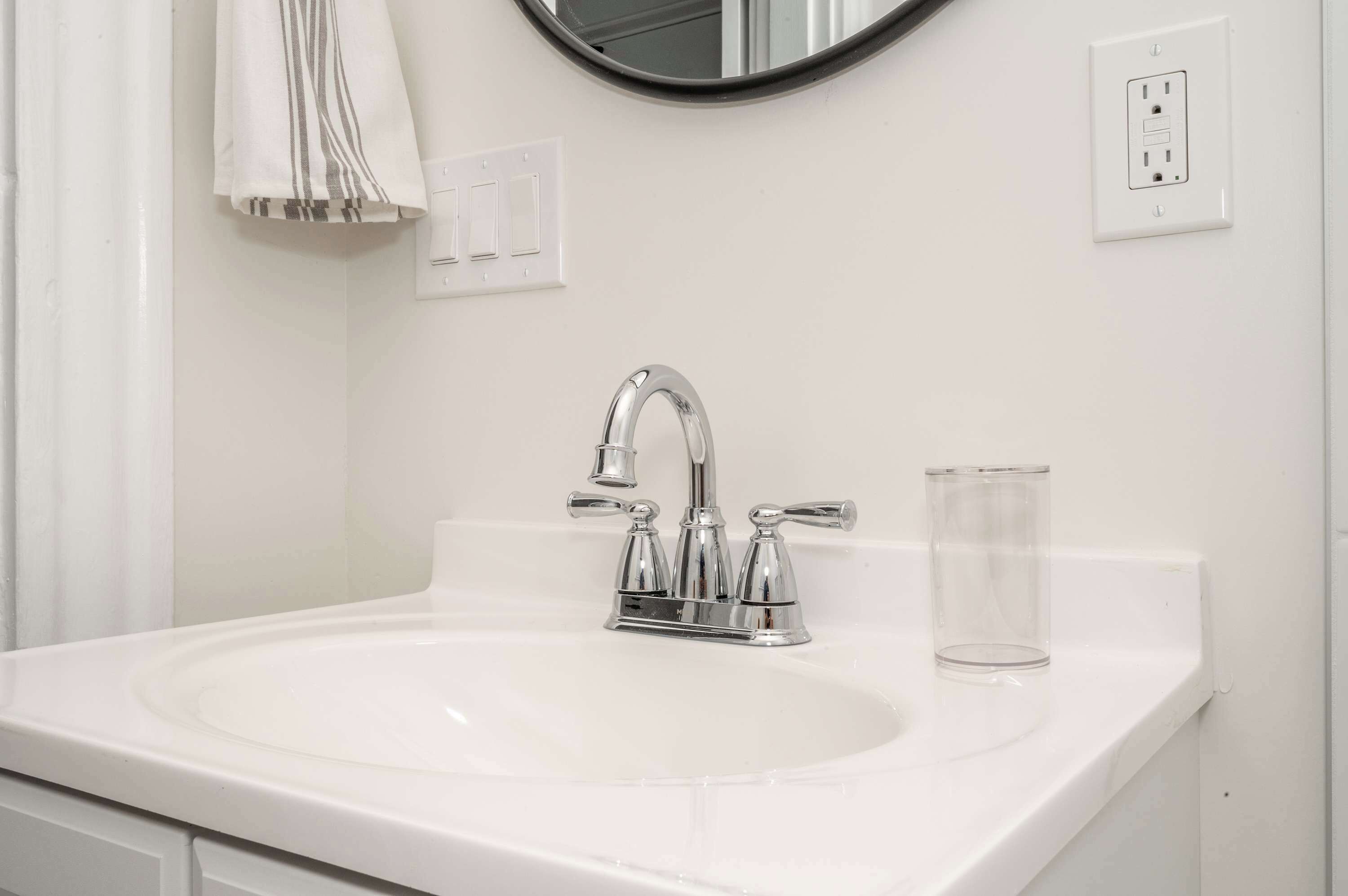 A white bathroom sink with a chrome faucet, a glass, and a towel hanging on the wall.