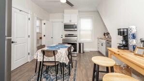 Una cocina compacta con muebles blancos, microondas, horno y un comedor con mesa y sillas.