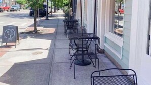Café al aire libre con mesas en la acera, sombrillas rojas y una pizarra.