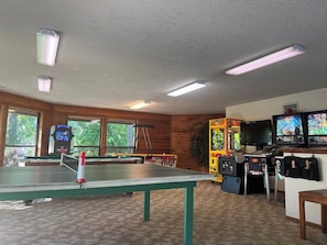 A room with a ping pong table, arcade games, and a pool table.