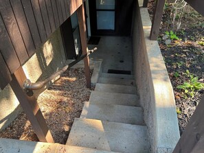 A concrete staircase leading to a wooden door, surrounded by gravel and mulch.