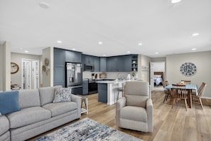 A modern kitchen with grey cabinets, a central island, and a dining area with a wooden table and chairs.