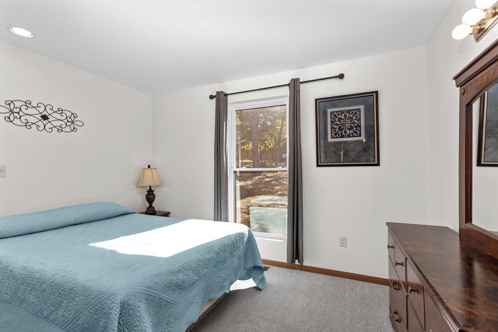 Une chambre à coucher comprenant un lit, une table de chevet, une commode, une fenêtre avec des rideaux et des œuvres d’art murales.