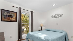 A bedroom with a bed, a window with curtains, a lamp, a wall decoration, and a framed picture.