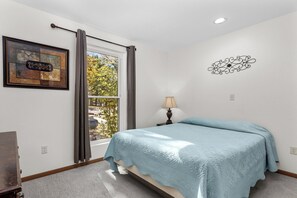 Ein Schlafzimmer mit einem Bett, einem Fenster mit Vorhängen, einer Lampe, einer Wanddekoration und einem gerahmten Bild.