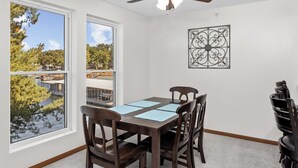 A dining area with a table, chairs, a ceiling fan, and a view of a body of water through large windows.