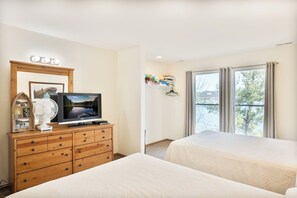 Habitación de hotel con dos camas, un televisor sobre una cómoda de madera, un ventanal con cortinas y vistas a árboles.