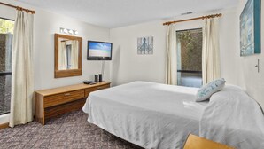 Una habitación de hotel con cama, televisión, cómoda y ventana con cortinas.