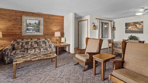 Una sala de estar acogedora con un sofá estampado, una silla de madera, una mesita y una lámpara.