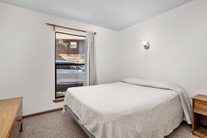 A bedroom with a bed, a nightstand, a window with a view of a parked car, and a wall-mounted light fixture. - Lone Oak Point 14 - Two Bedroom Apartment, Sleeps 6 (Sunrise Beach)