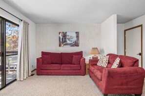 A living room with two red sofas, a painting on the wall, a lamp, and a door. - Lone Oak Point 14 - Two Bedroom Apartment, Sleeps 6 (Sunrise Beach)