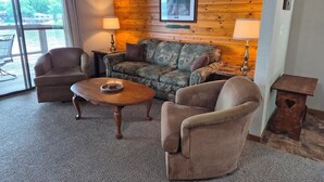 A room with a wooden wall, a sofa, two armchairs, a coffee table, and a lamp.