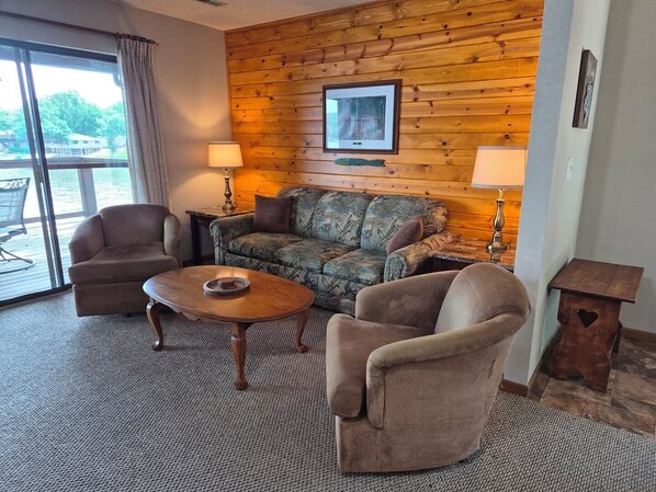A room with a wooden wall, a sofa, two armchairs, a coffee table, and a lamp.