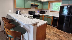 A modern kitchen with green cabinets, a marble countertop, a black refrigerator, and a built-in oven.