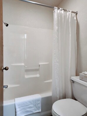 A bathroom with a shower, toilet, and a towel on the floor.