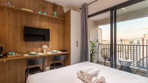 A modern hotel room with a large bed, a desk with chairs, a flat-screen TV, and a balcony with a city view. - Studio Facto - São Paulo (São Paulo)