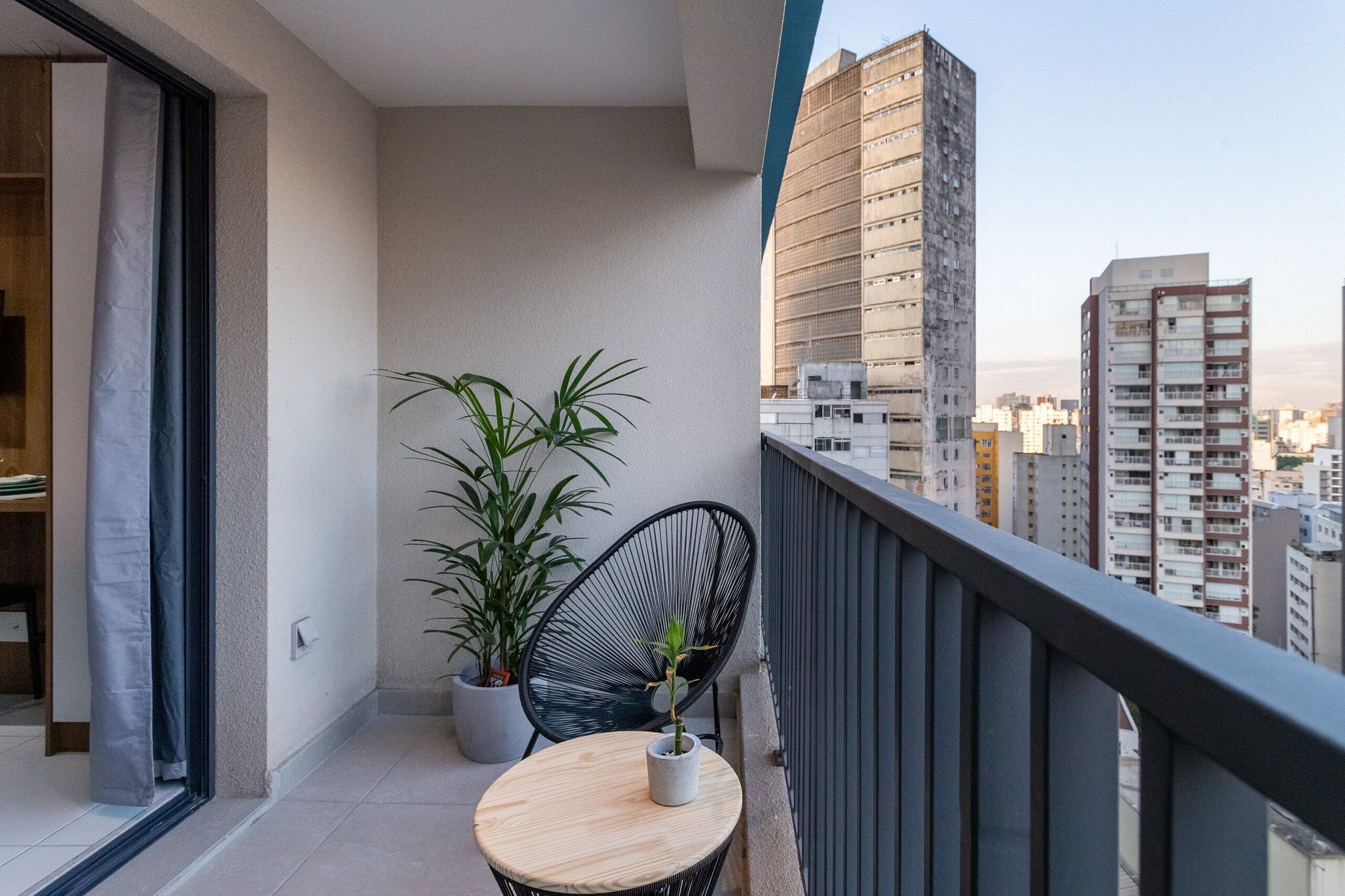 Un balcon avec une table ronde et deux chaises, un pot de fleurs et une vue sur de hauts immeubles.