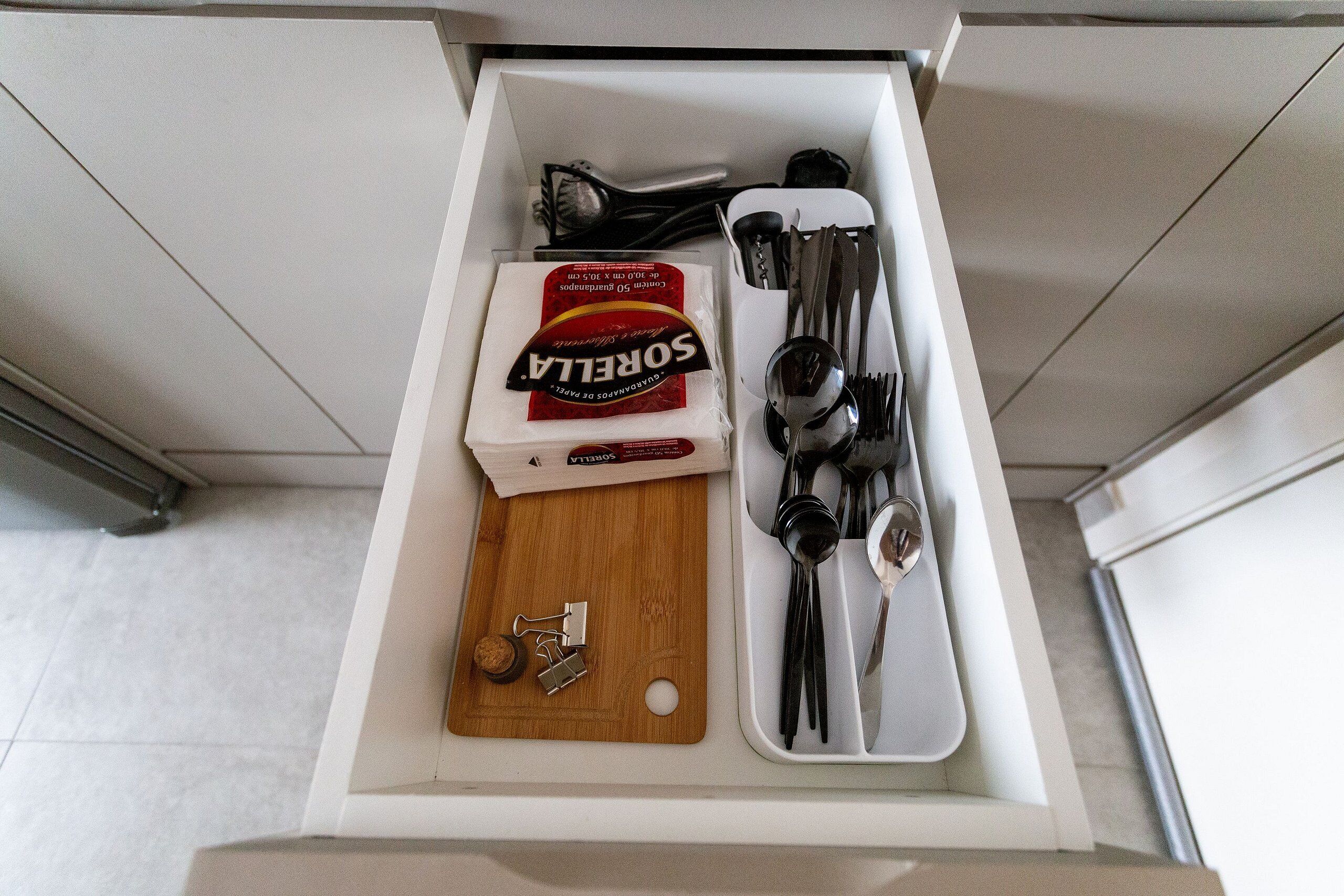 A drawer containing a wooden cutting board, a box of Sorel pasta, and various kitchen utensils.