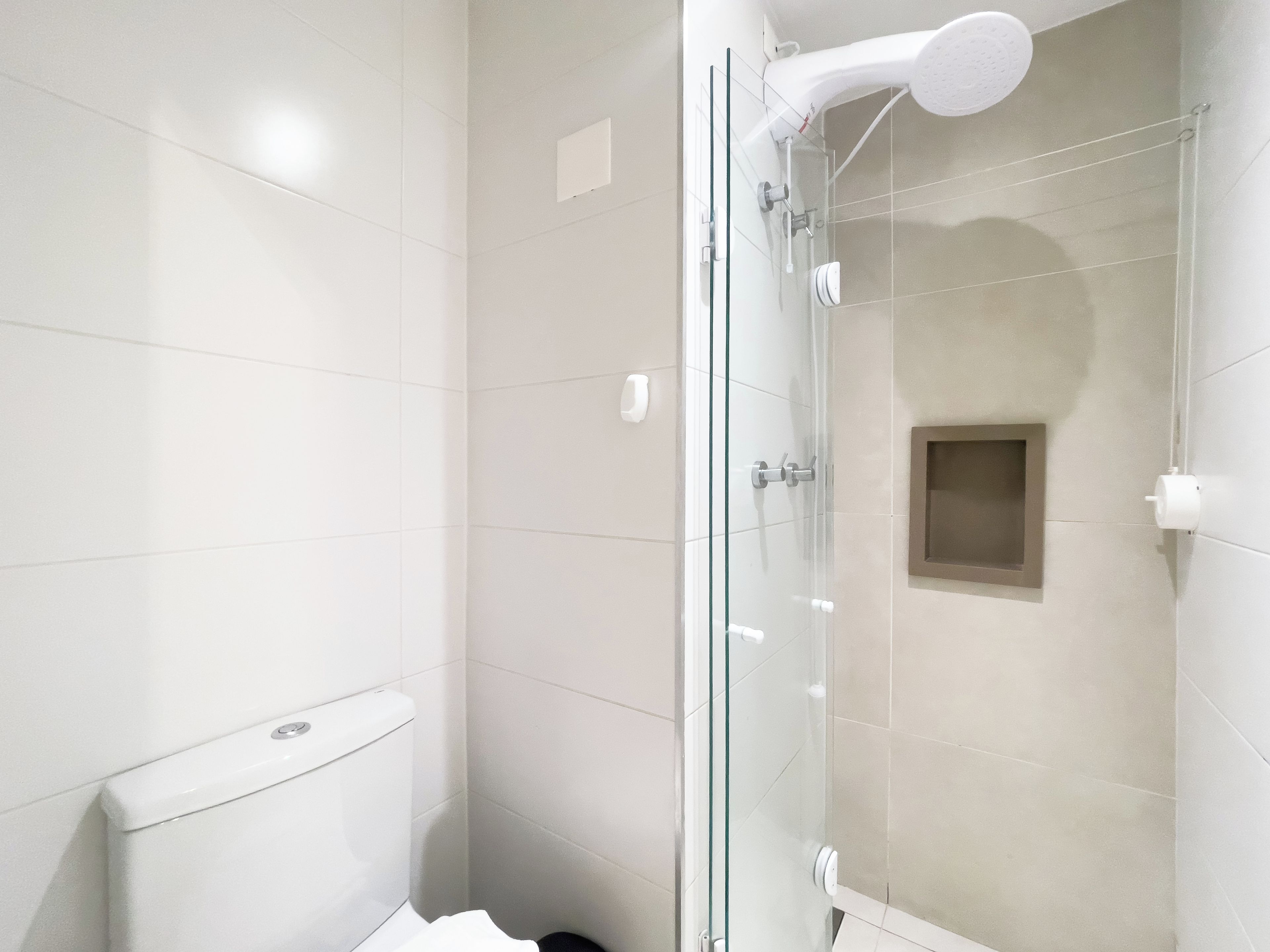 Un baño moderno con ducha envuelta en vidrio, azulejos blancos y un inodoro.