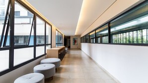 A modern corridor with large windows, grey ottomans, and a staircase in the distance. - Studio Facto - São Paulo (São Paulo)