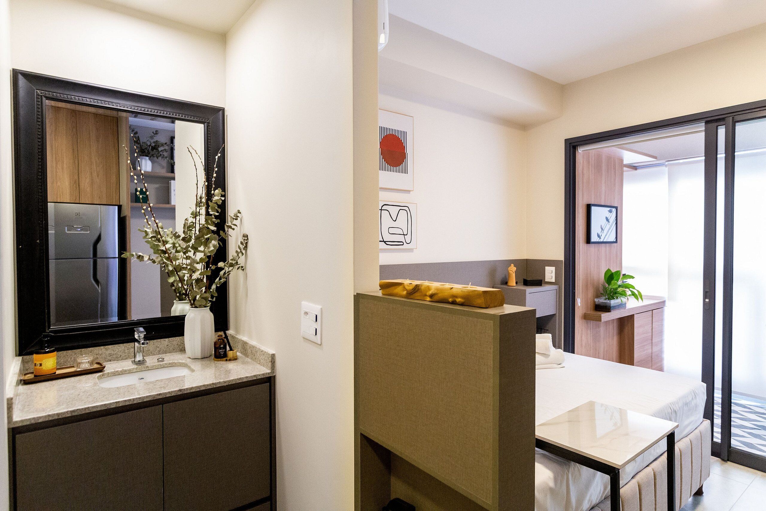 A modern bathroom with a large mirror, a sink, and a toilet. There is a plant on the counter and a shower area visible through the glass door.