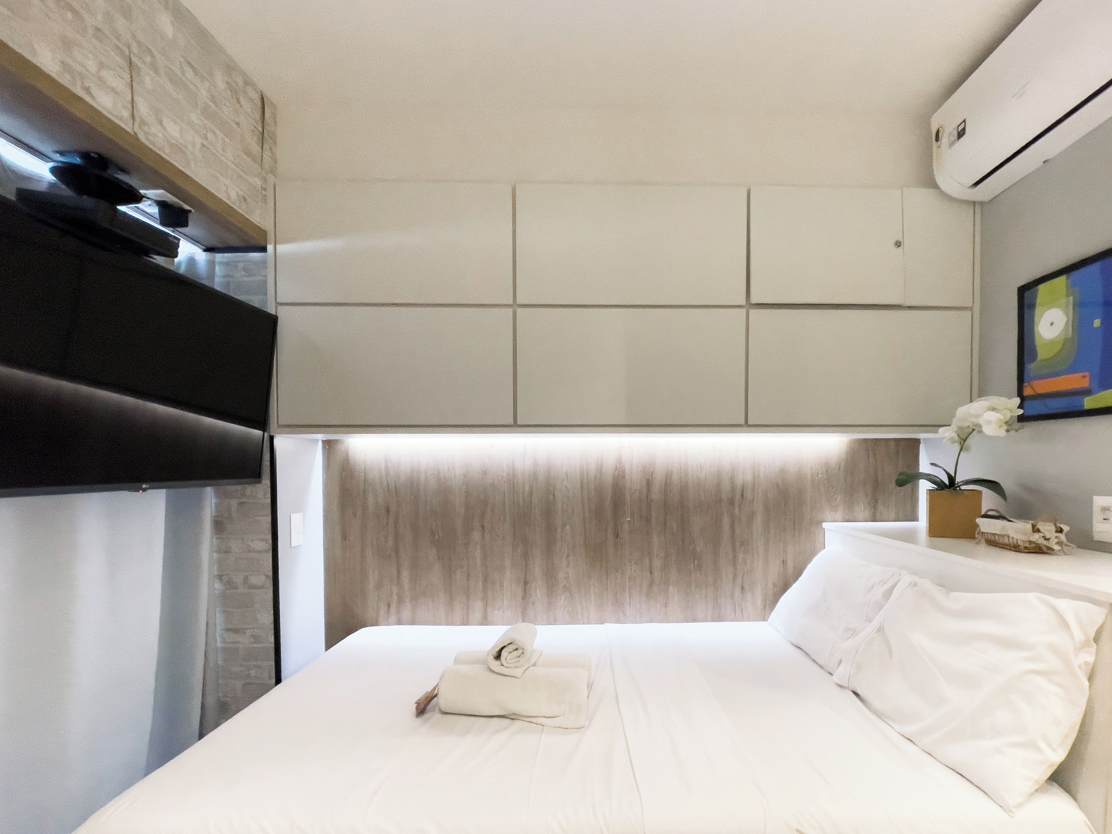 Een hotelkamer met een bed, een flatscreen televisie, een wandairconditioner en een schilderij.
