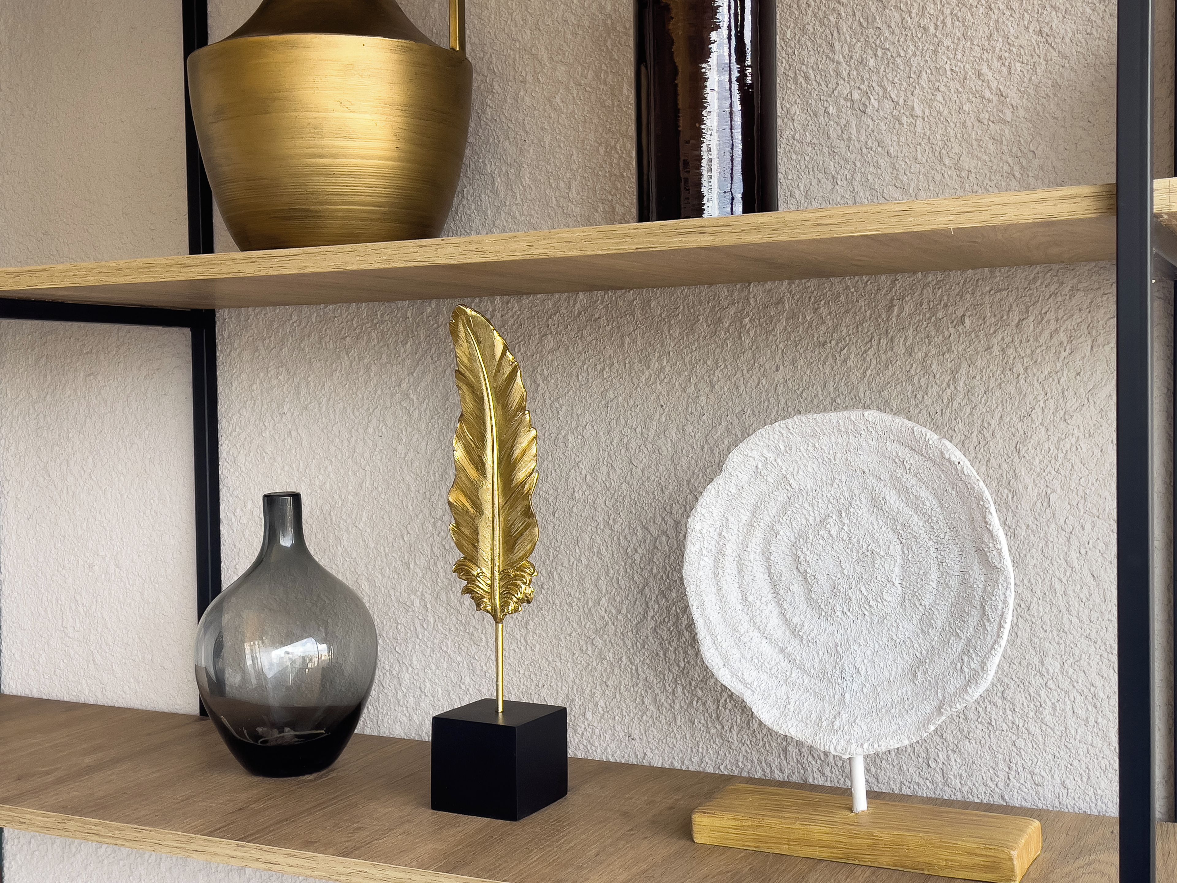 A shelf with a gold vase, a black vase, and a golden feather decoration.