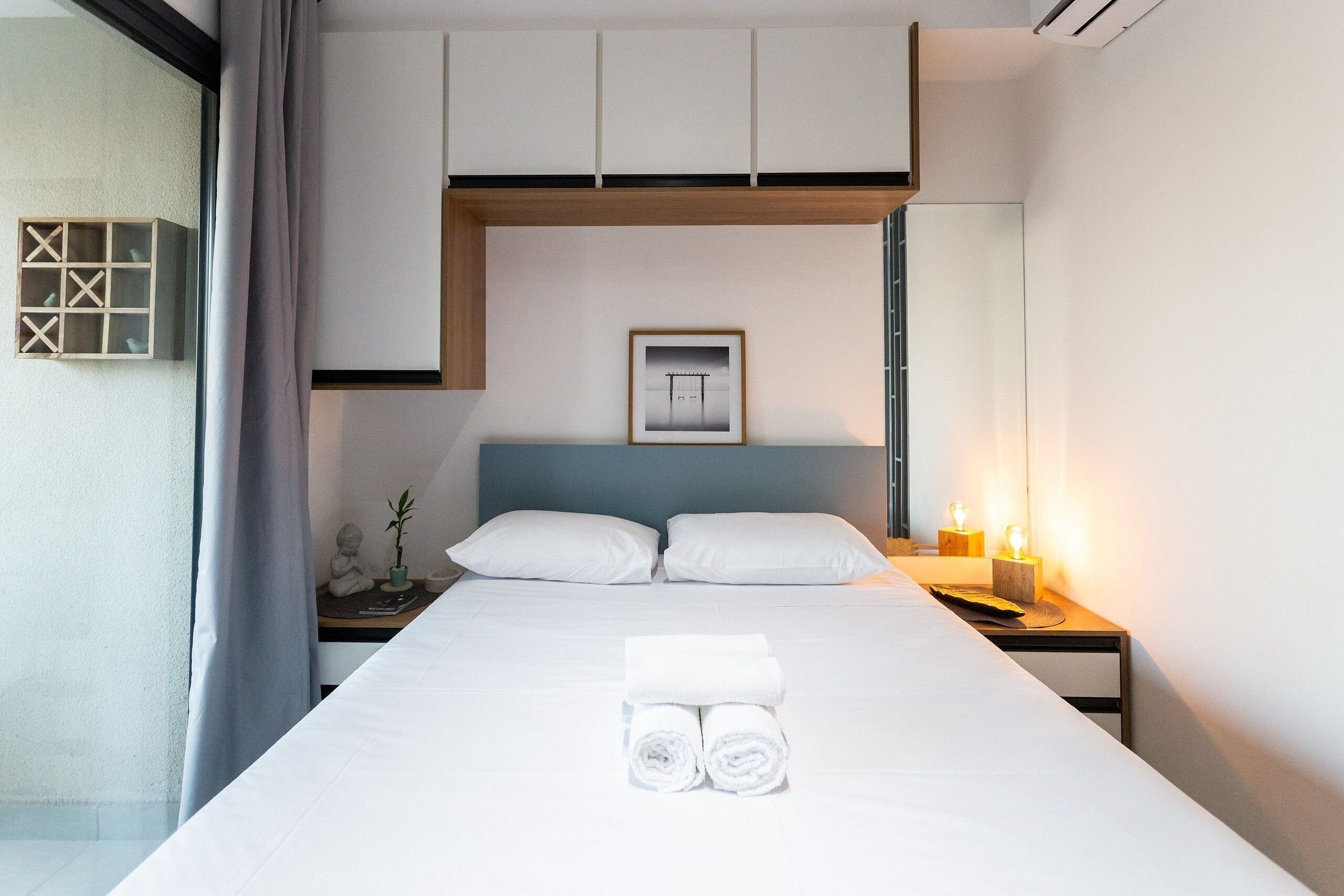 Une chambre d’hôtel moderne avec un lit bien fait, deux oreillers, une table de chevet avec une lampe et une étagère murale agrémentée d’objets décoratifs.