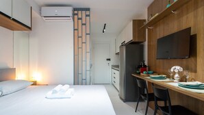 A hotel room with a bed, a desk, a TV, and a kitchen area. - Studio Facto - São Paulo (São Paulo)