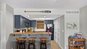 Una cocina con armarios azul oscuro, una isla de madera con taburetes y un refrigerador con papeles encima.