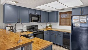 Una cocina con armarios azul oscuro, un refrigerador negro, un microondas, una estufa y una encimera de madera.