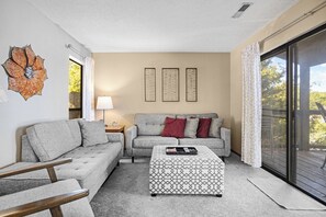Una sala de estar con sofá, sillón, mesa de centro, lámpara y un elemento decorativo en la pared.