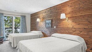 Una habitación con dos camas, paneles de madera en las paredes, un ventanal y dos lámparas fijadas a la pared.