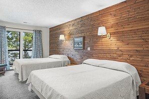 Quarto com duas camas, paredes em painel de madeira, janela com vista e duas luminárias fixadas na parede.