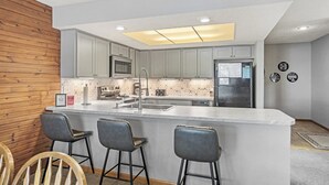 Una cocina moderna con una isla central, taburetes de bar y una pared de acento de madera.