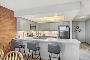 A modern kitchen with a central island, bar stools, and a wooden accent wall. - Lone Oak Point 31 - Three Bedroom Apartment, Sleeps 8 (Sunrise Beach)