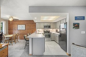 A modern kitchen with a central island, wooden wall paneling, and a 'Welcome to our lake house' sign. - Lone Oak Point 31 - Three Bedroom Apartment, Sleeps 8 (Sunrise Beach)