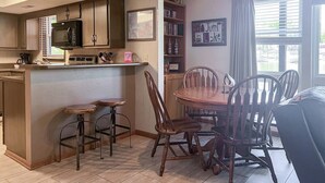 A kitchen with a microwave, a coffee maker, and a bar area. There is a dining table with chairs and a ceiling fan.