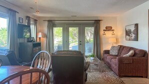 A living room with a sofa, a dining table with chairs, a ceiling fan, and a television.