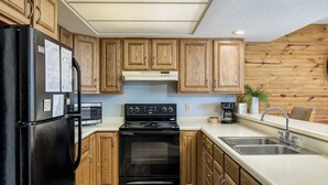 Une cuisine avec des meubles de rangement en bois, un réfrigérateur noir, une cuisinière, un four à micro-ondes et un évier.