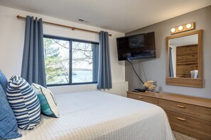 A bedroom with a bed, a TV, a dresser, and a window with curtains.