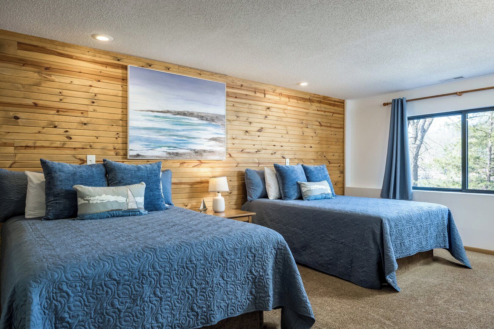 Habitación de hotel con dos camas, una pared de madera, un cuadro y una ventana con cortinas.