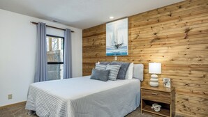 Une chambre à coucher avec un lit, une table de chevet avec une lampe, un panneau mural en bois et une fenêtre avec des rideaux.