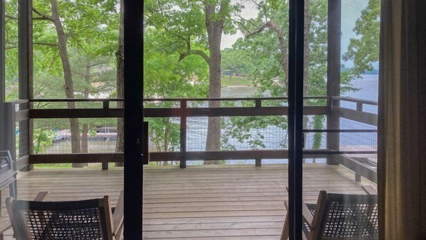 Une terrasse en bois avec deux chaises et une table, donnant sur une étendue d’eau et des arbres.