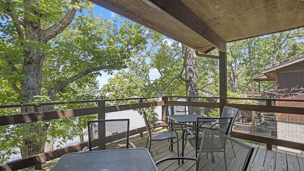 Une terrasse extérieure couverte, dotée de tables et de chaises, qui offre une vue sur un plan d’eau et des arbres.