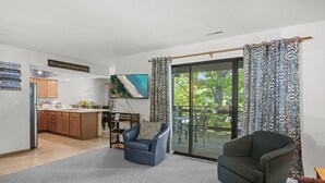Un salon comprenant un canapé, un fauteuil, un téléviseur et une porte-fenêtre coulissante donnant sur une terrasse.